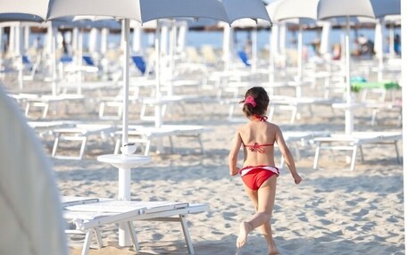 A beach with rows of white lounge chairs and umbrellas, a sandy beach, and a clear view of the sea.