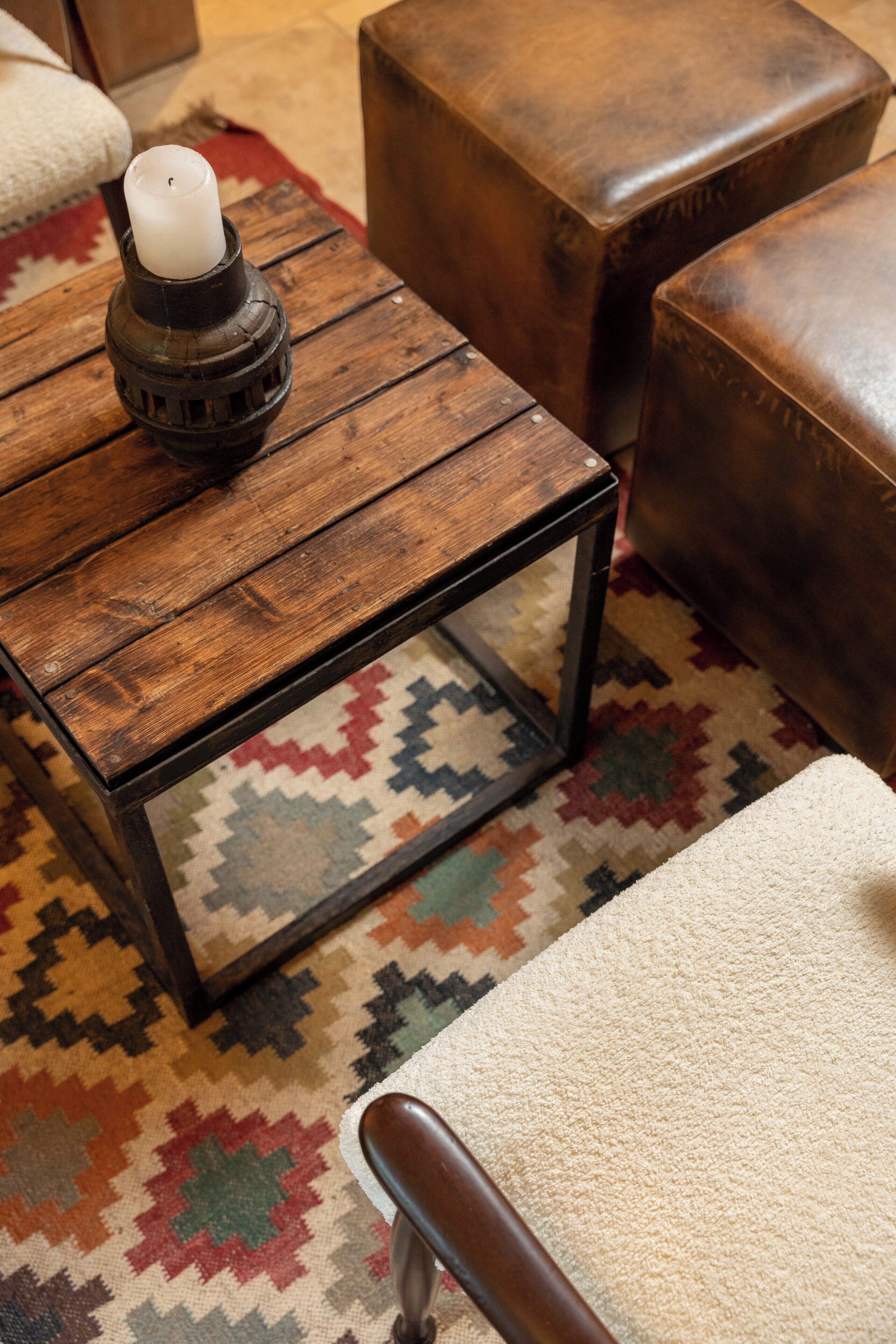 A wooden coffee table with a candle, a patterned rug, and leather ottomans.