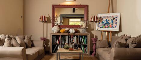 A living room with a sofa, a coffee table, a bookshelf, a painting, and a mirror.