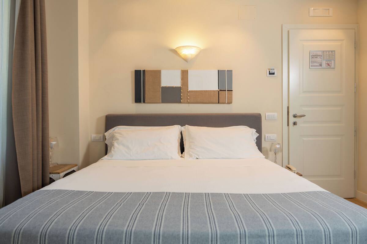 A neatly made bed with a striped bedspread, a wall-mounted light fixture, and a door with a notice on it.