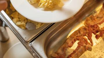 A buffet with scrambled eggs and bacon on a plate.