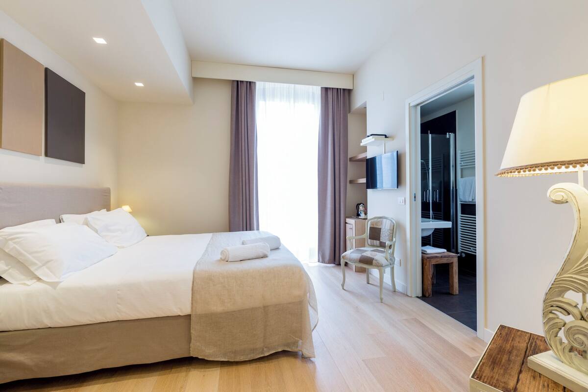 A hotel room with a bed, a chair, a desk, and a bathroom visible through an open door.