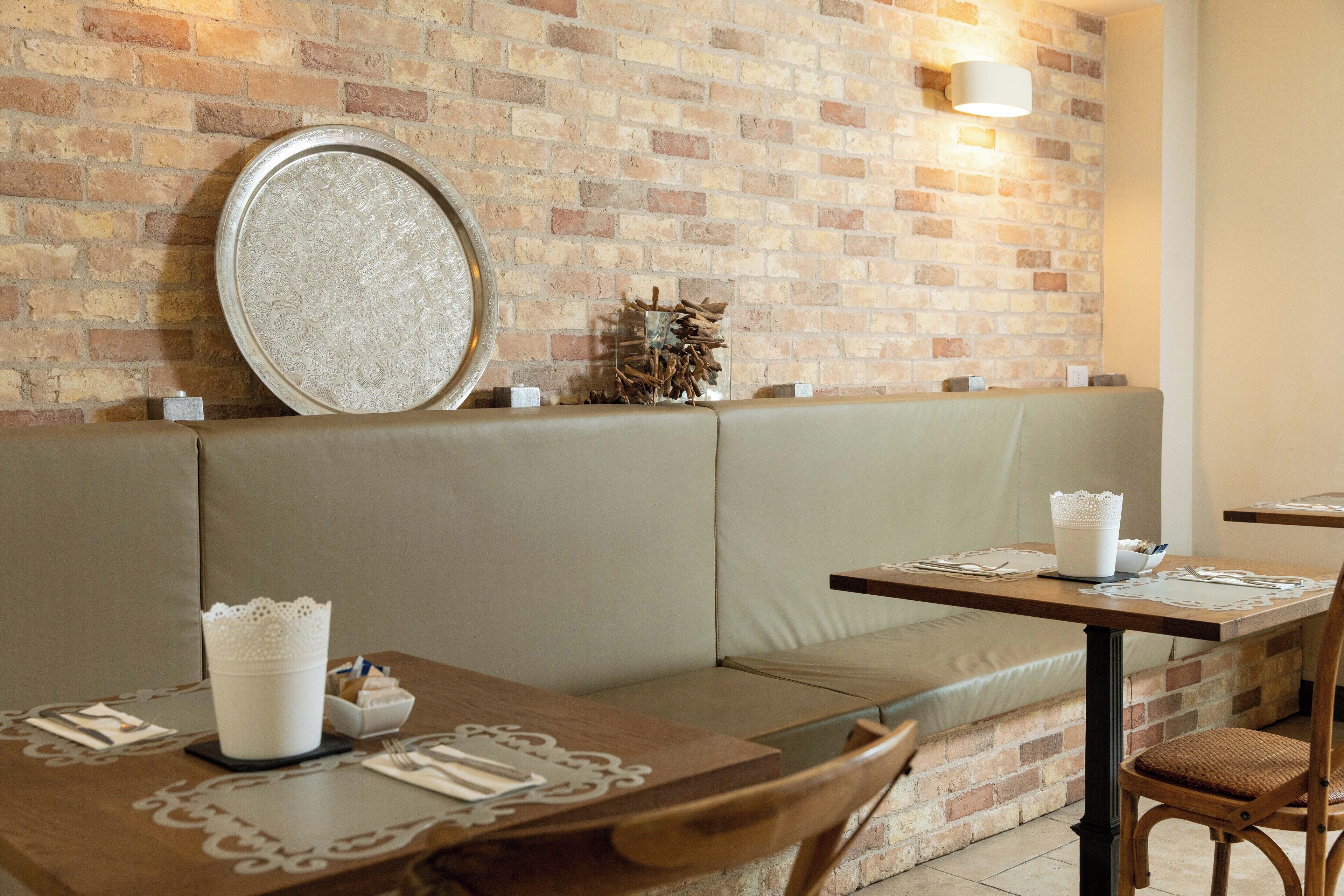 A restaurant with a brick wall, cushioned seating, and tables set with white tableware.