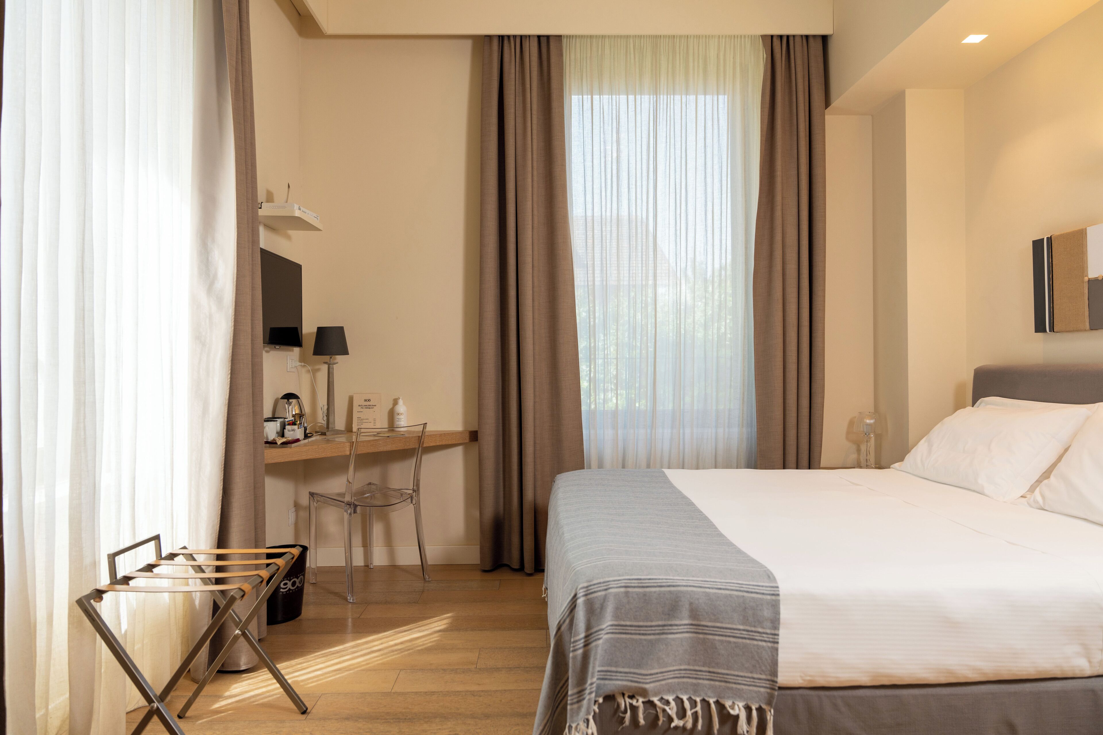 Habitació d'hotel amb un llit, una taula de treball, una cadira i una finestra amb cortines.
