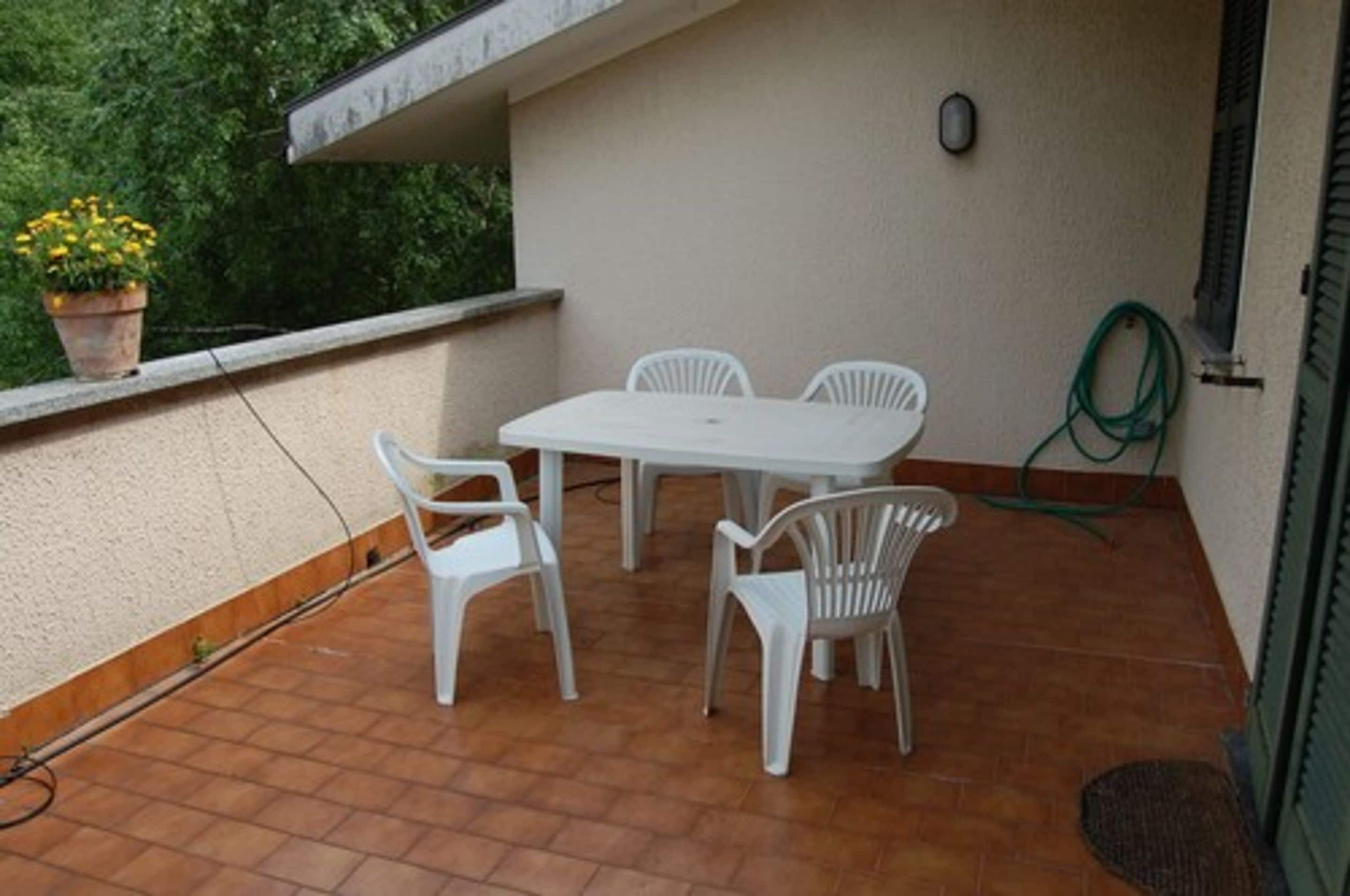 A small outdoor patio with a white table and four chairs, a potted plant, and a hose on the ground.