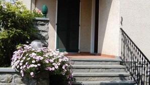 A building with a stone staircase leading to a black door, a stone planter with pink flowers, and a black railing. - Bed and Breakfast Casa Nini (Lierna)