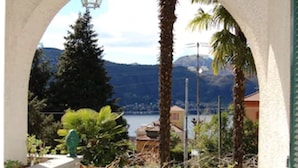 A balcony with a view of a lake and mountains, a chair, and a hanging light fixture. - Bed and Breakfast Casa Nini (Lierna)