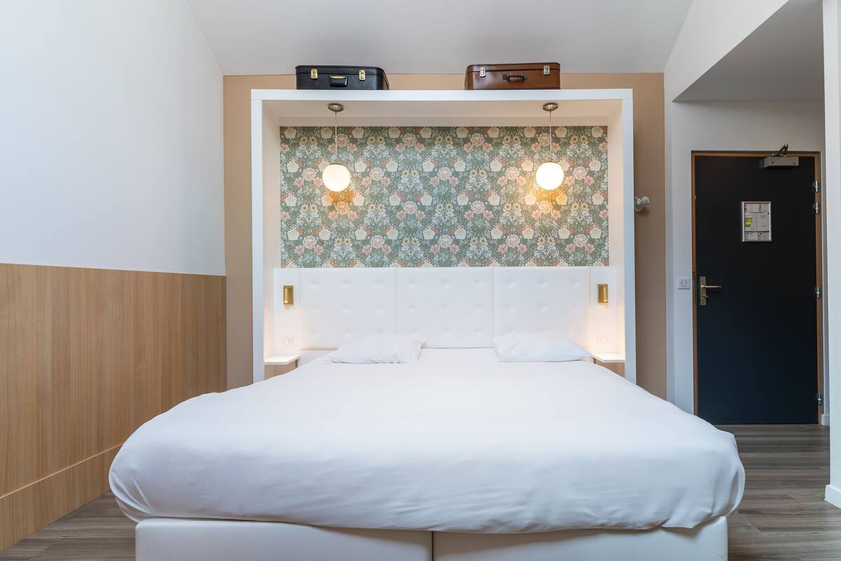 A modern hotel room with a large bed, two bedside lamps, a floral-patterned headboard, and a wooden accent wall.