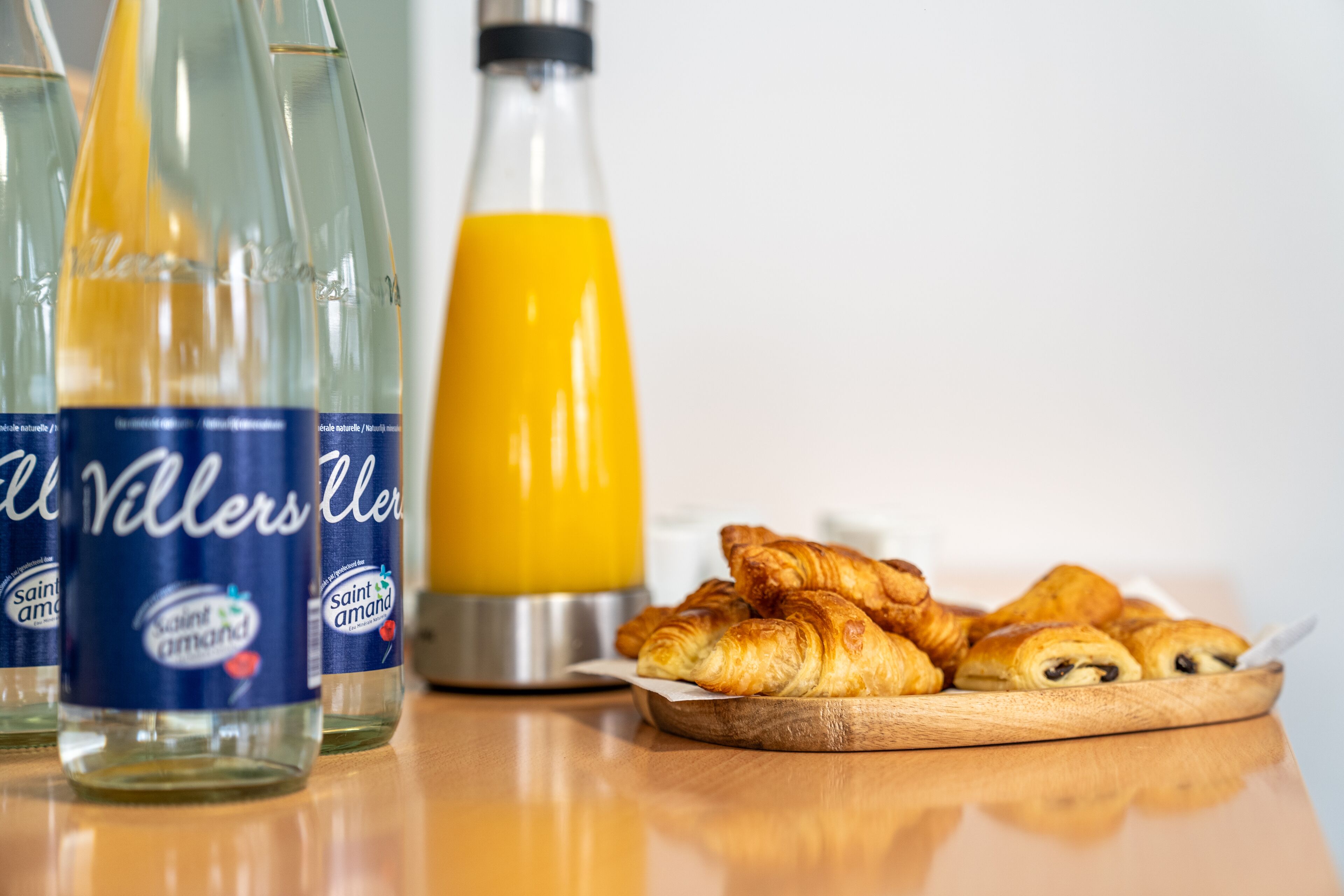 Bottles of Saint Amant juice, a glass of orange juice, and a plate of croissants.