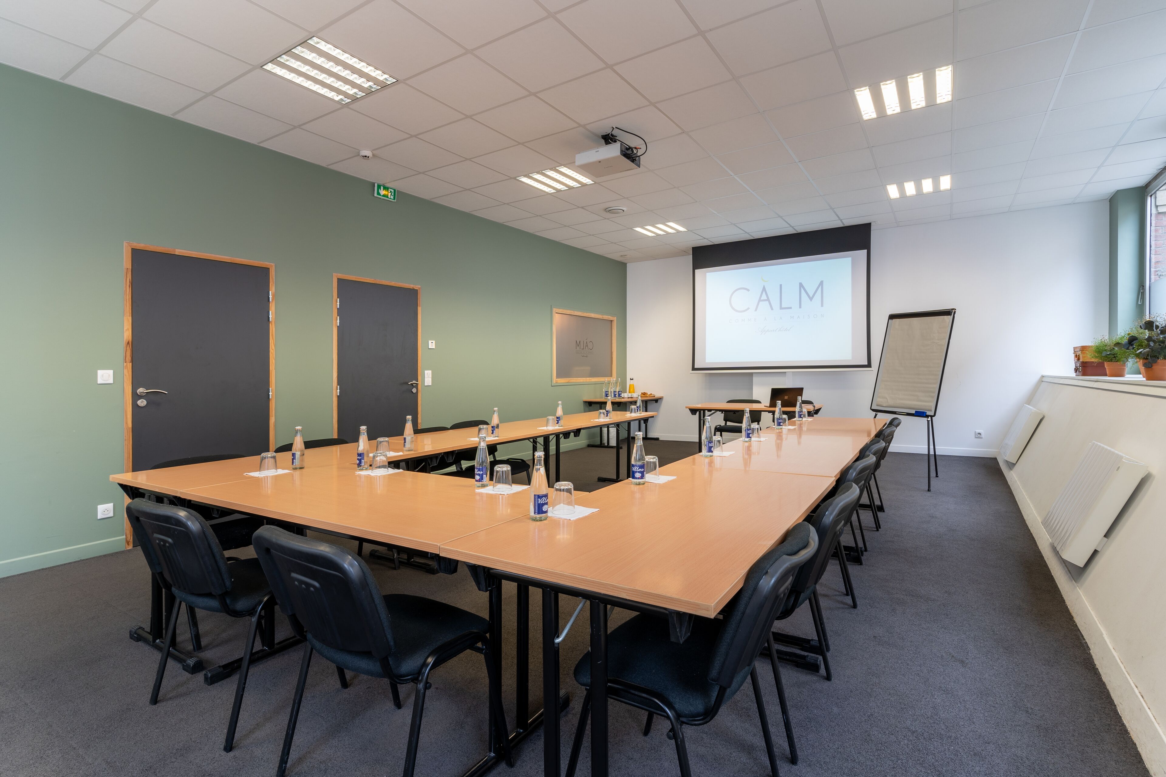 A conference room with a long table, black chairs, a projector screen, and a whiteboard.