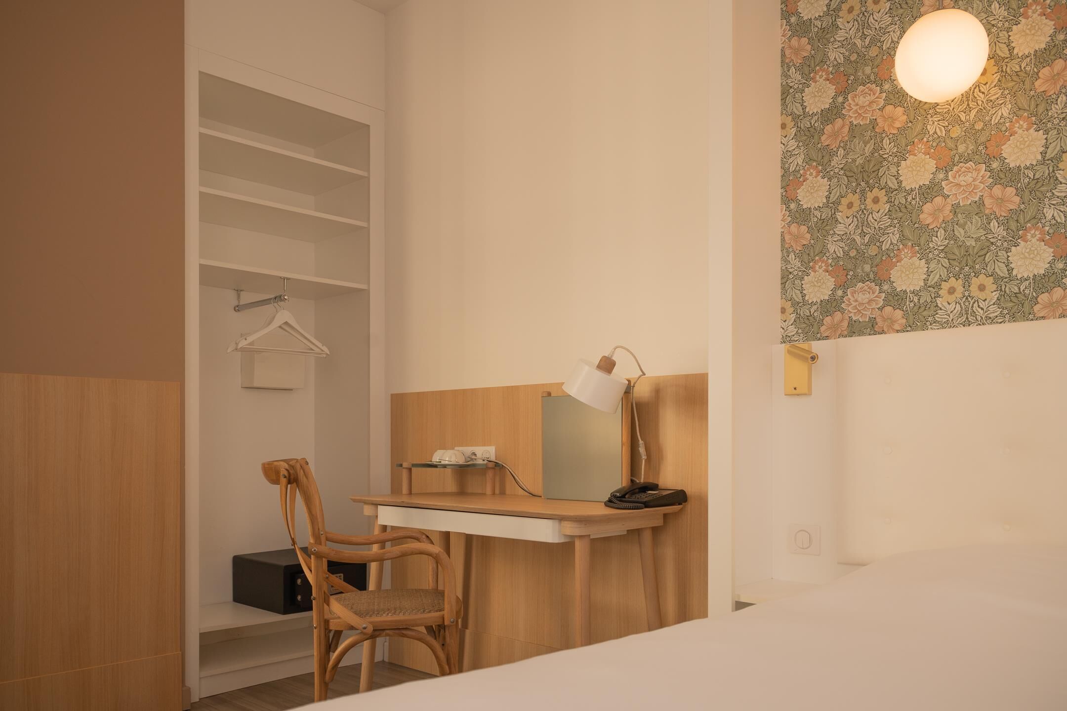 Een hotelkamer met een houten bureau, een stoel, een kapstok en een wandlamp.