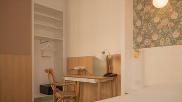 Een hotelkamer met een houten bureau, een stoel, een kapstok en een wandlamp.