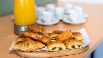 Een houten dienblad met croissants en een gele beker, waarschijnlijk voor sap, op een tafel. Op de achtergrond witte kopjes en schotels.