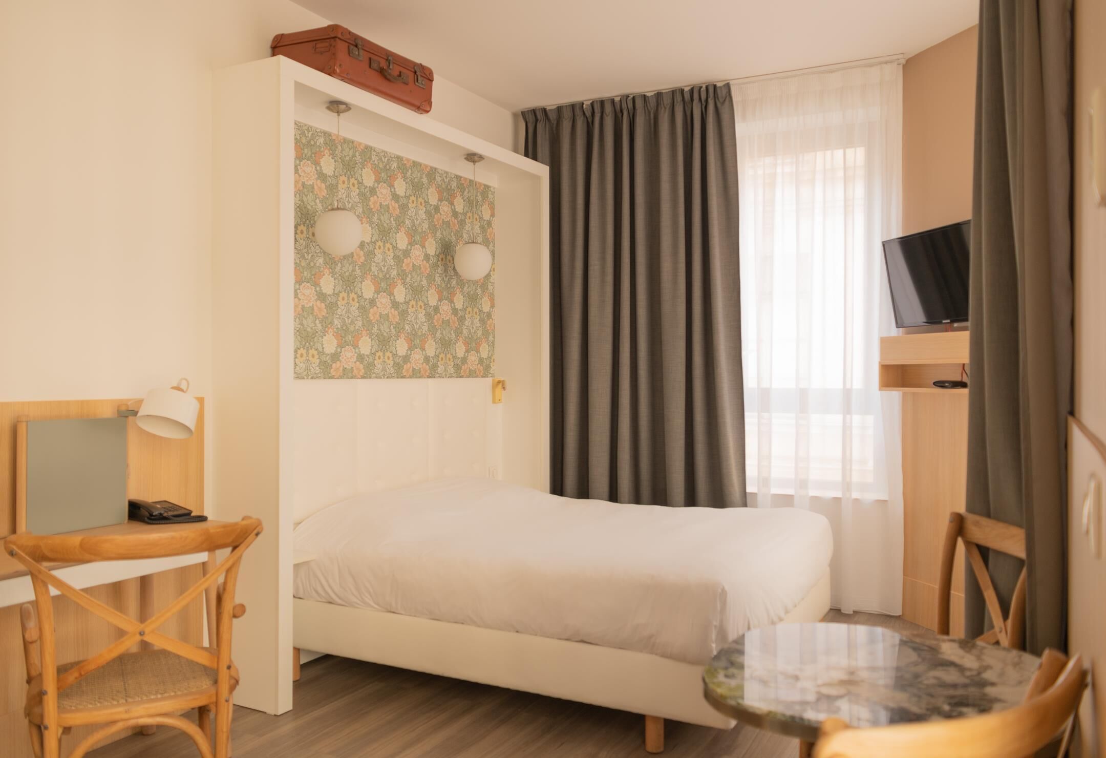 A bedroom with a bed, a desk with a lamp, a television, and a small table.
