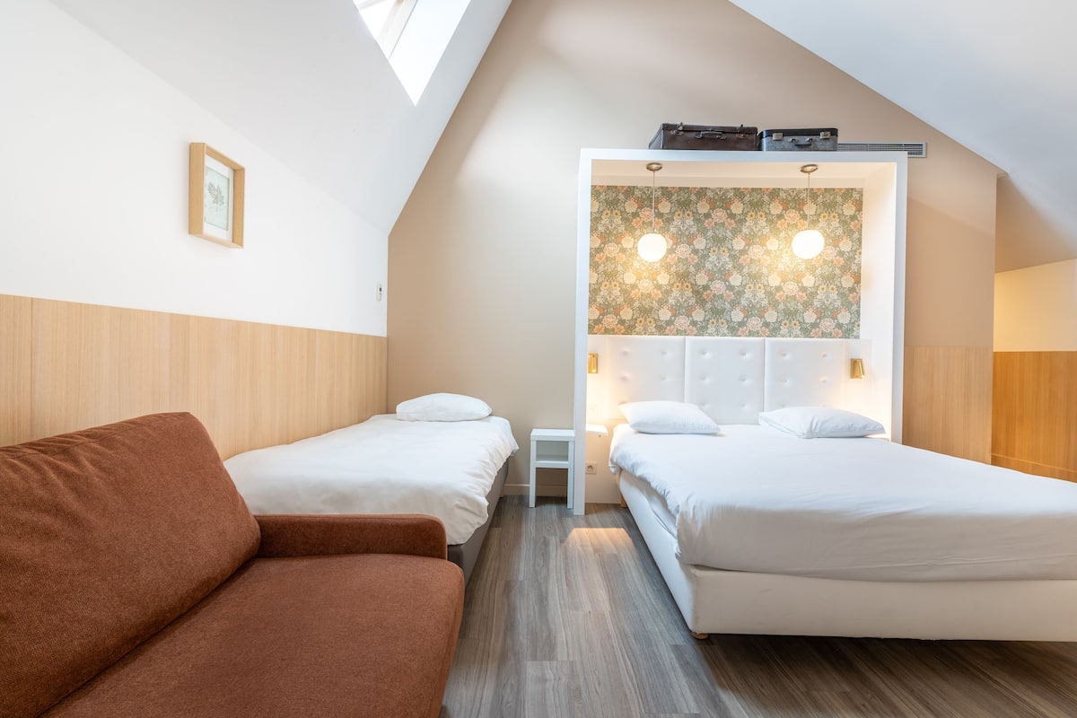 A bedroom with two single beds, a brown sofa, and a skylight.