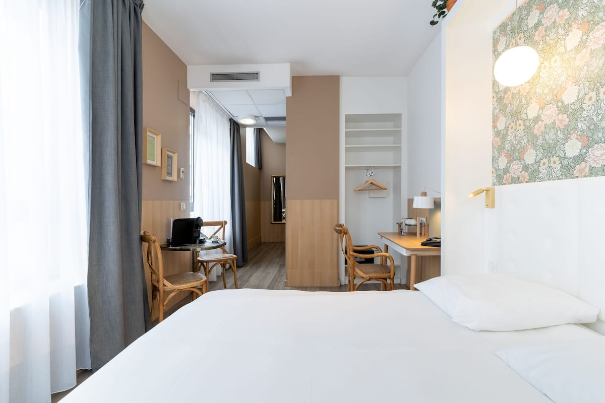 A hotel room with a bed, a desk, two chairs, a wardrobe, and a bathroom visible through an open door.