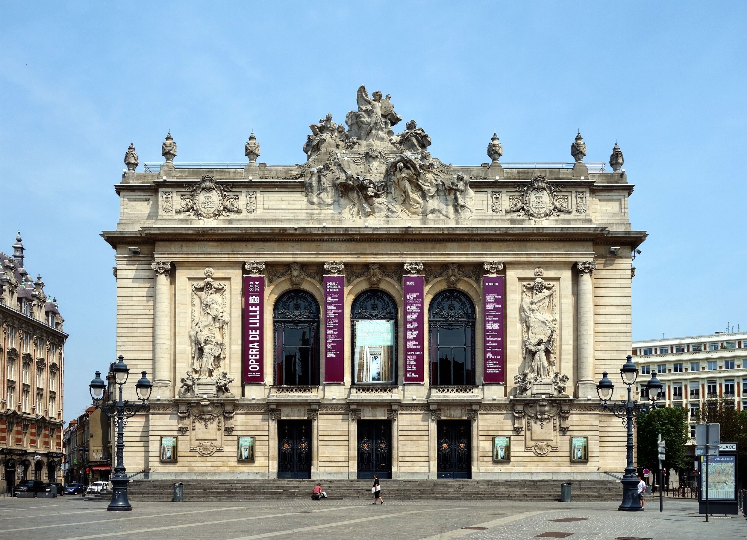 Un edificio histórico con esculturas ornamentales, amplias ventanas en arco y pancartas que anuncian eventos.
