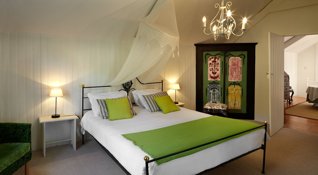Un dormitorio con una cama grande, dos mesitas de noche con lámparas, una silla verde y una puerta decorativa con obras de arte.