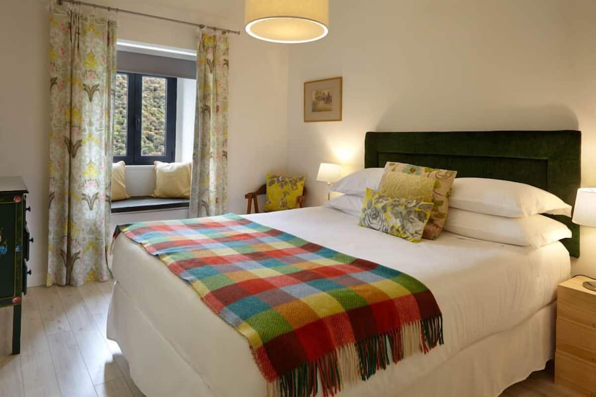 A neatly arranged bedroom with a large bed, a bedside table, a lamp, and a window with curtains.