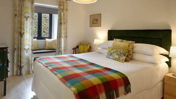 Un dormitorio ordenado con una cama grande, una mesita de noche, una lámpara y una ventana con cortinas.