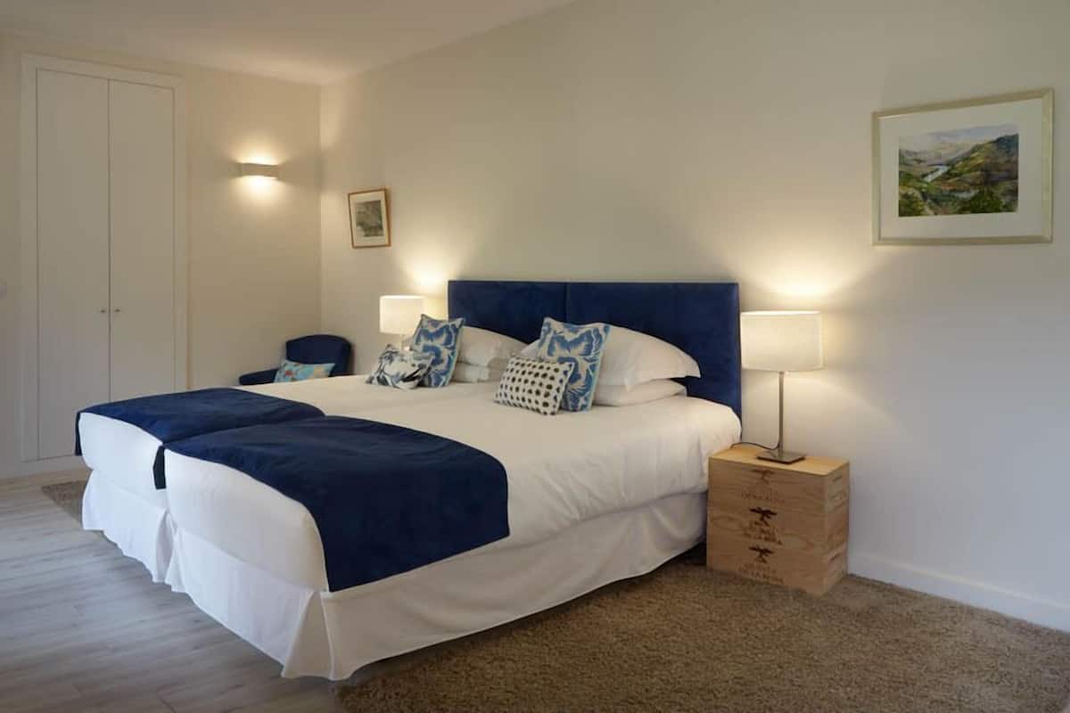A bedroom with a large bed, two bedside lamps, a wooden nightstand, and a door.