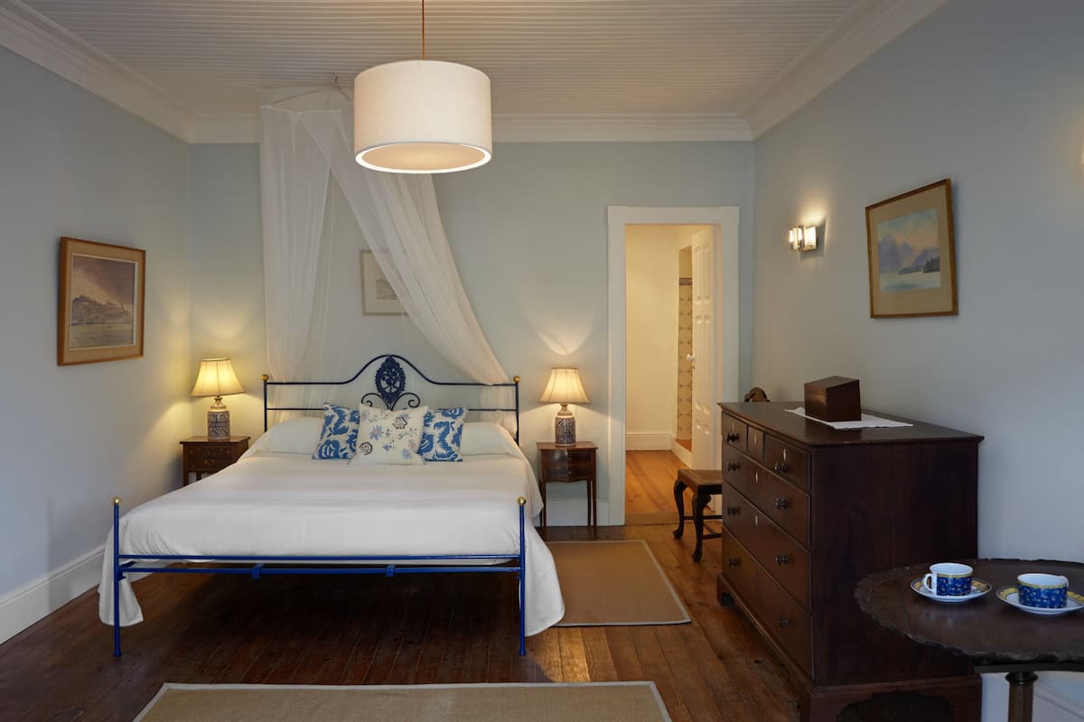 A bedroom with a bed, bedside lamps, a dresser, a table with cups, and a painting on the wall.