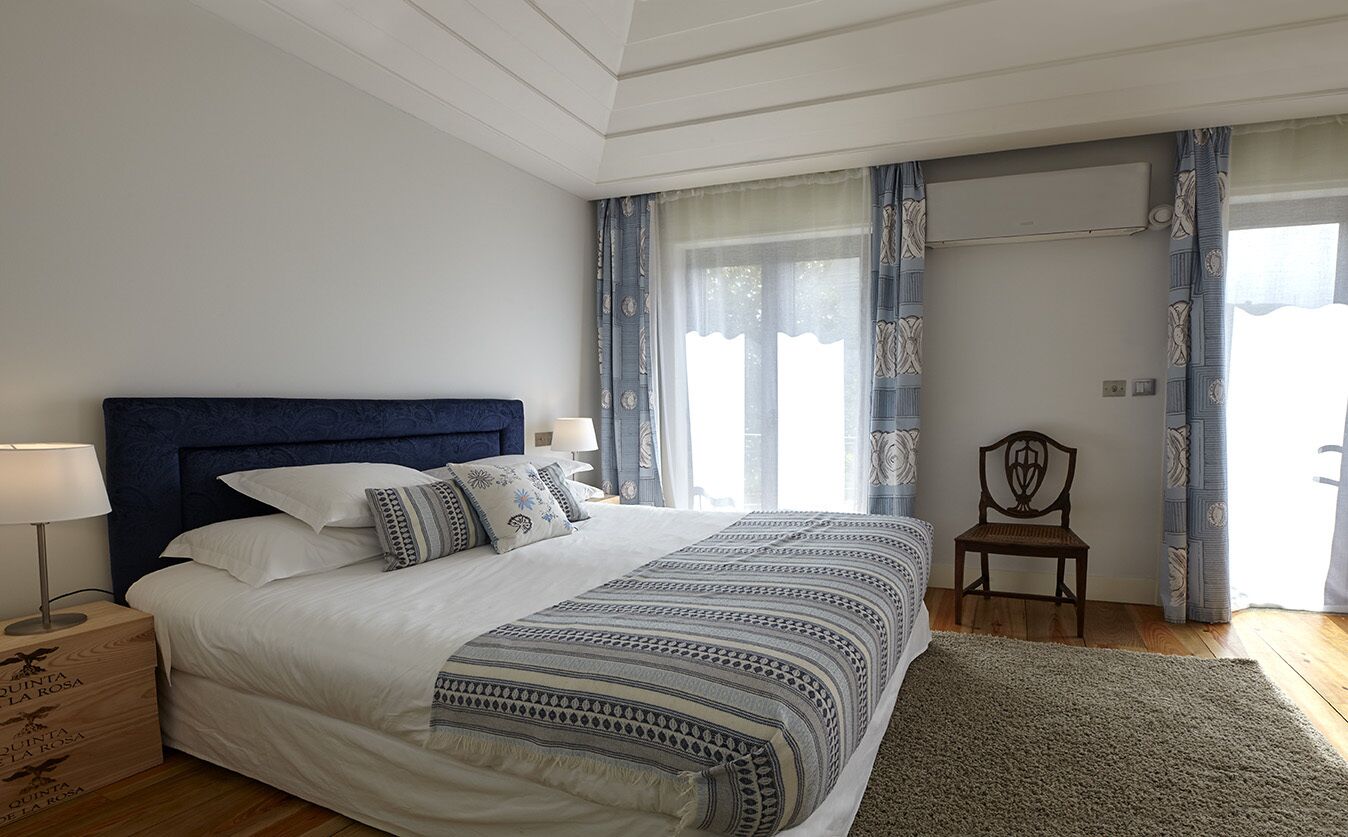 A bedroom with a large bed, a nightstand, a chair, and a window with curtains.