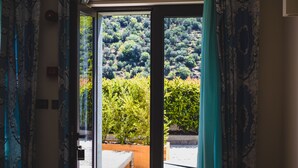 A doorway leading to a balcony with a view of a hillside.