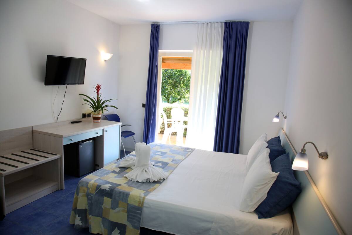 Une chambre d’hôtel équipée d’un lit, d’un bureau, d’une télévision et offrant une vue sur l’extérieur.
