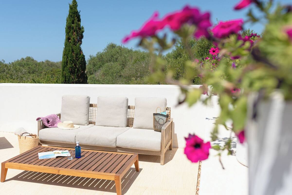 A white outdoor seating area with a wooden table, a woven basket, and a bottle.