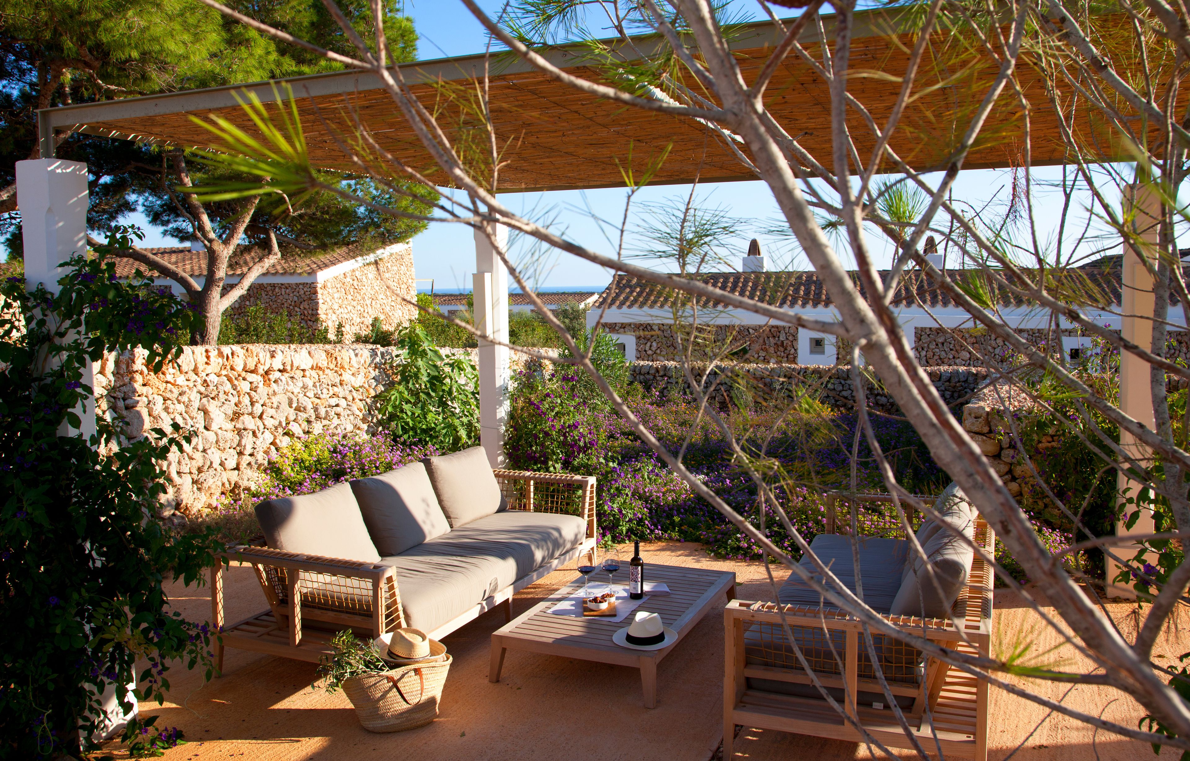 Een terras met buitenmeubilair, een stenen muur, een houten pergola en een uitzicht op huizen op de achtergrond.