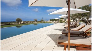 Zona de piscina con sillones y sombrillas, cielo despejado y vista al mar.