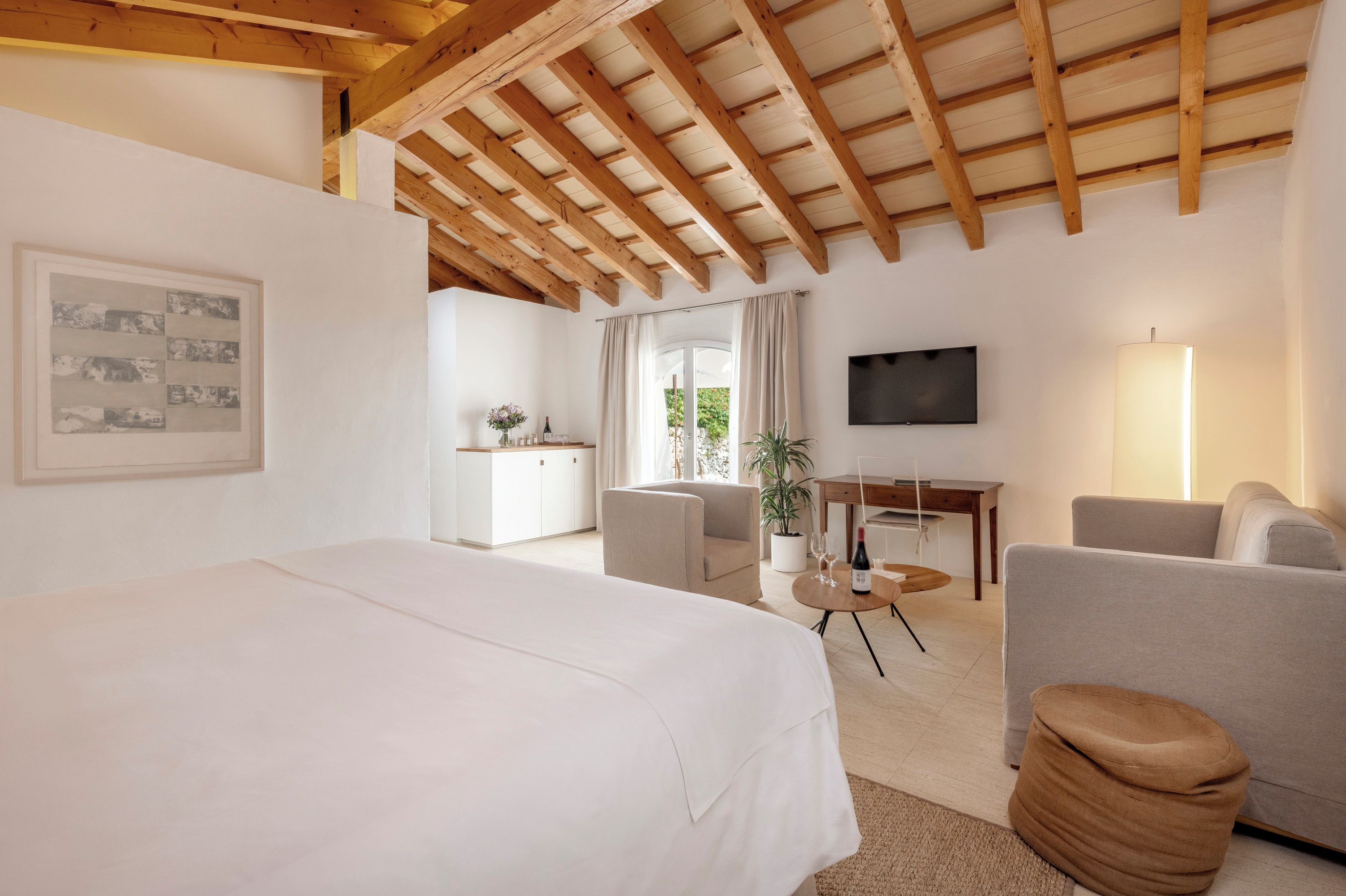 Une chambre d’hôtel avec un grand lit, un bureau, une télévision et un coin salon agrémenté d’une plante.