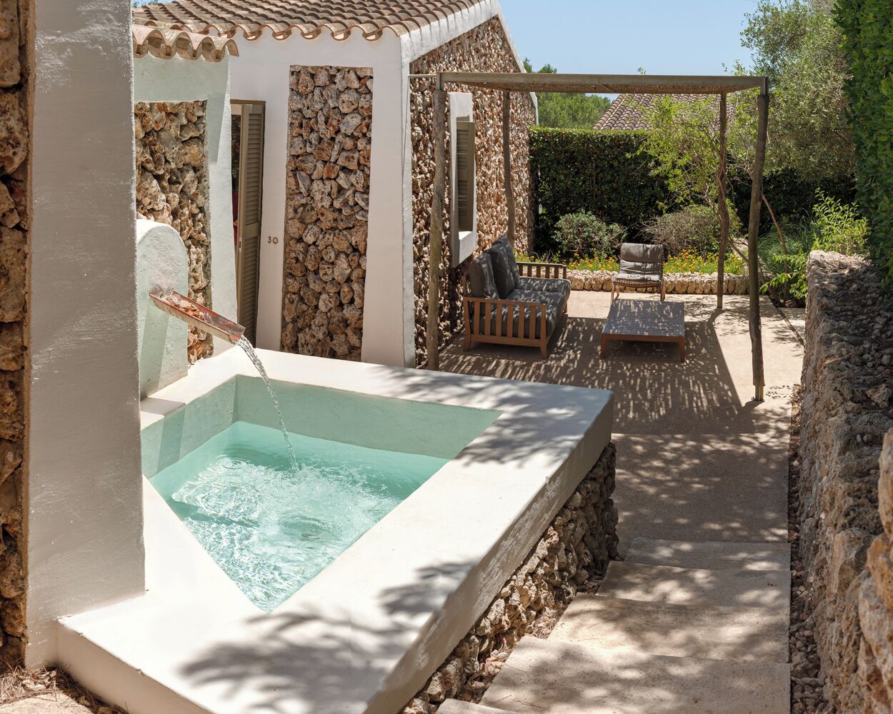Een buitenzwembad met een stenen muur, een pergola en zitplaatsen.