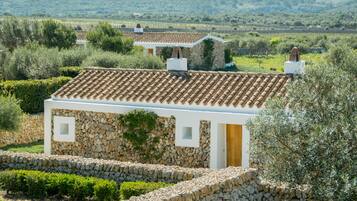 A stone building with a tiled roof, surrounded by greenery and olive trees.