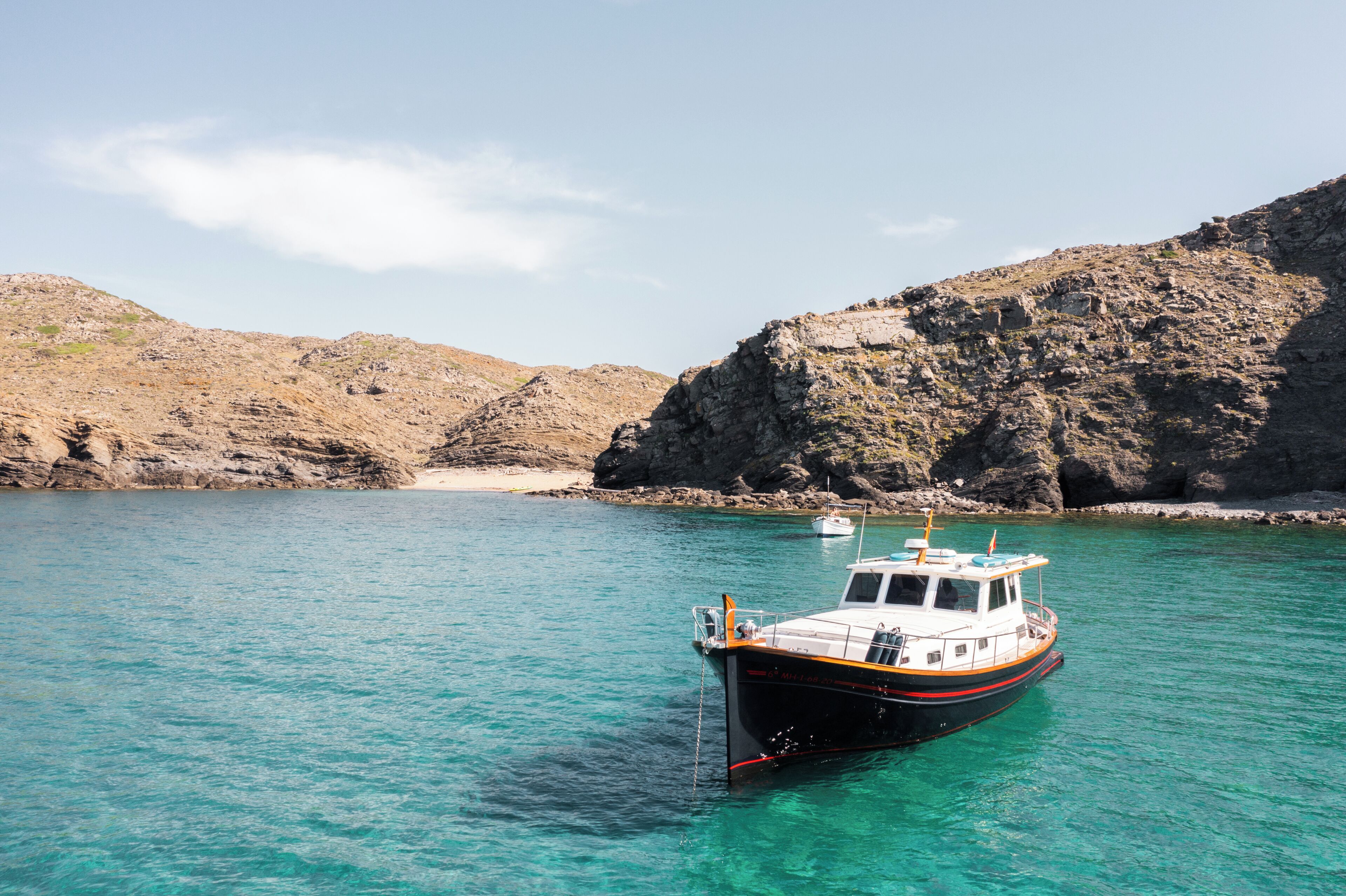 Un bateau est ancré dans une eau turquoise et limpide, avec des collines rocheuses en arrière-plan.