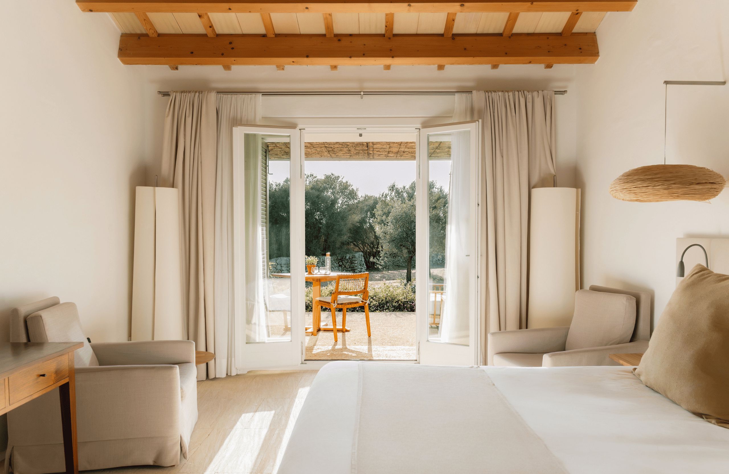 Ein Hotelzimmer mit Bett, zwei Stühlen, einem Schreibtisch und Blick auf einen Garten durch eine offene Tür.