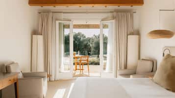 Ein Hotelzimmer mit Bett, zwei Stühlen, einem Schreibtisch und Blick auf einen Garten durch eine offene Tür.