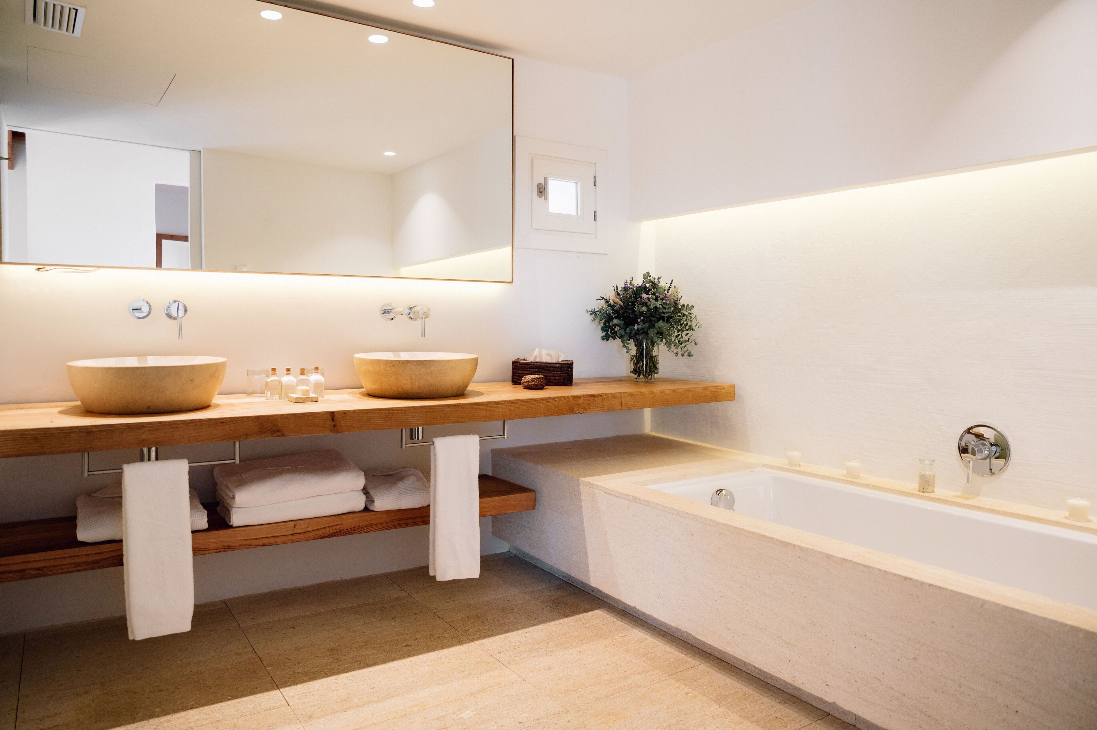A modern bathroom with two large sinks, a large mirror, a bathtub, and a small plant.