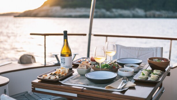 Una mesa de comedor en un barco con diversos platos, copas y una botella de vino.