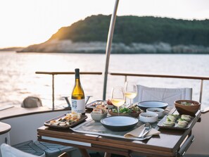 Una mesa de comedor en un barco con diversos platos, copas y una botella de vino.