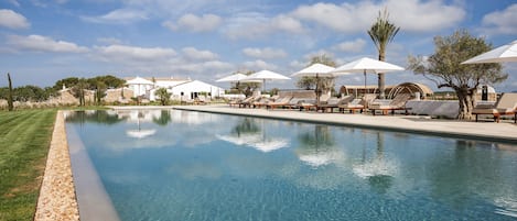 Una piscina al aire libre, sombrillas, sillones reclinables de piscina