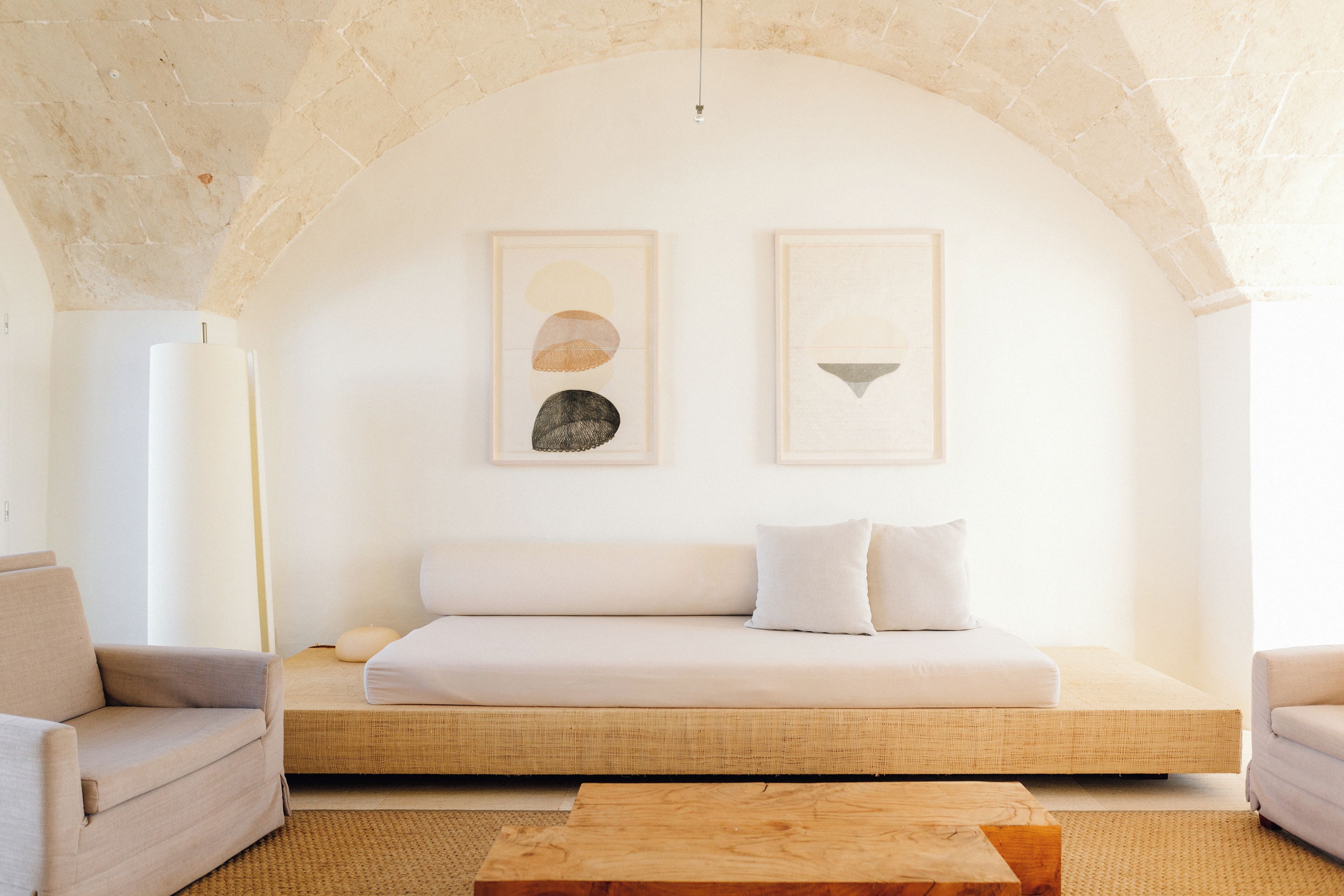 A minimalist room with a low ceiling, a sofa, a wooden coffee table, and two framed artworks on the wall.