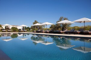 Una piscina al aire libre, sombrillas, sillones reclinables de piscina