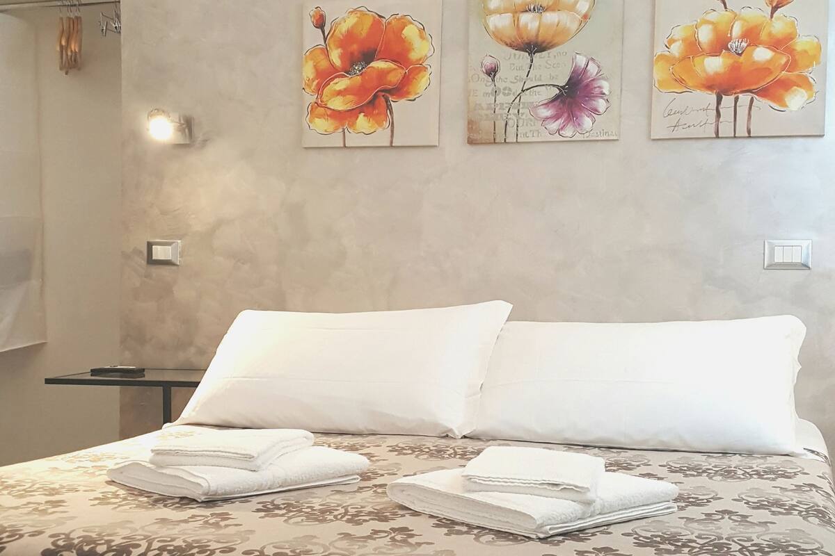 Ein ordentlich bezogenes Bett mit weißen Laken und einer gesteppten Decke in einem Zimmer mit strukturierter Wand.