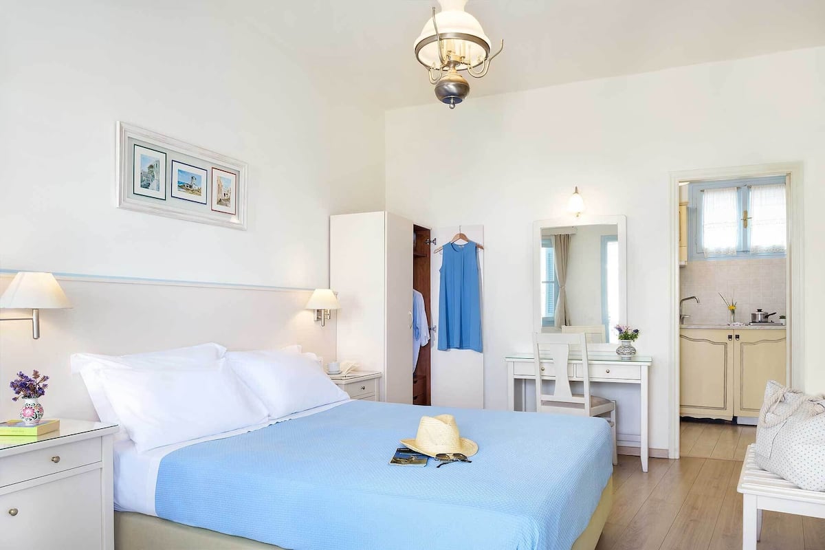 A hotel room with a bed, bedside tables, a desk, a mirror, and a kitchenette.
