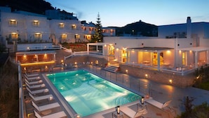 A poolside area with lounge chairs and a swimming pool, surrounded by buildings with outdoor lighting. - Perigiali Hotel (Skiros)