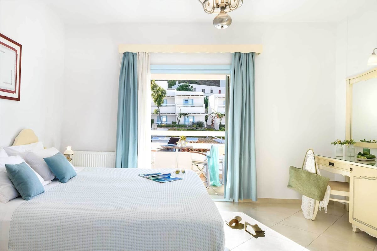 A bedroom with a bed, a dresser, a mirror, and a view of buildings outside.