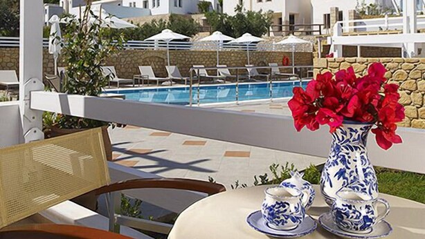 A terrace with a pool, white buildings in the background, and a table with a vase of flowers. - Perigiali Hotel (Skiros)