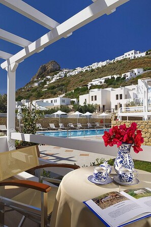 A terrace with a pool, white buildings in the background, and a table with a vase of flowers. - Perigiali Hotel (Skiros)